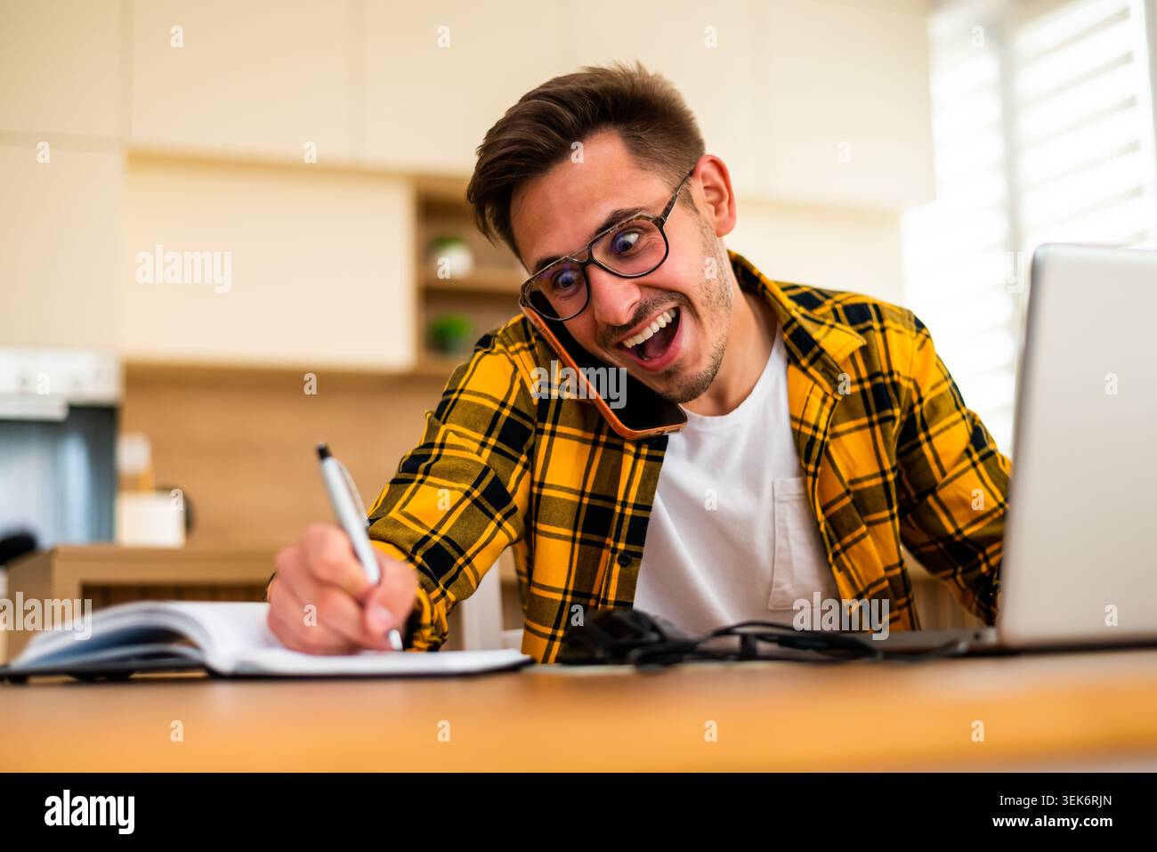 Lavorando da casa, un giovane sta scrivendo idee e promemoria, combinando la ricerca online con il tradizionale prendere appunti. Foto Stock