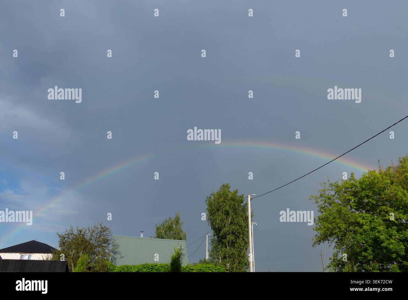Doppio arcobaleno nel cielo buio e tempestoso dopo la pioggia. Paesaggio di campagna con alberi verdi Foto Stock