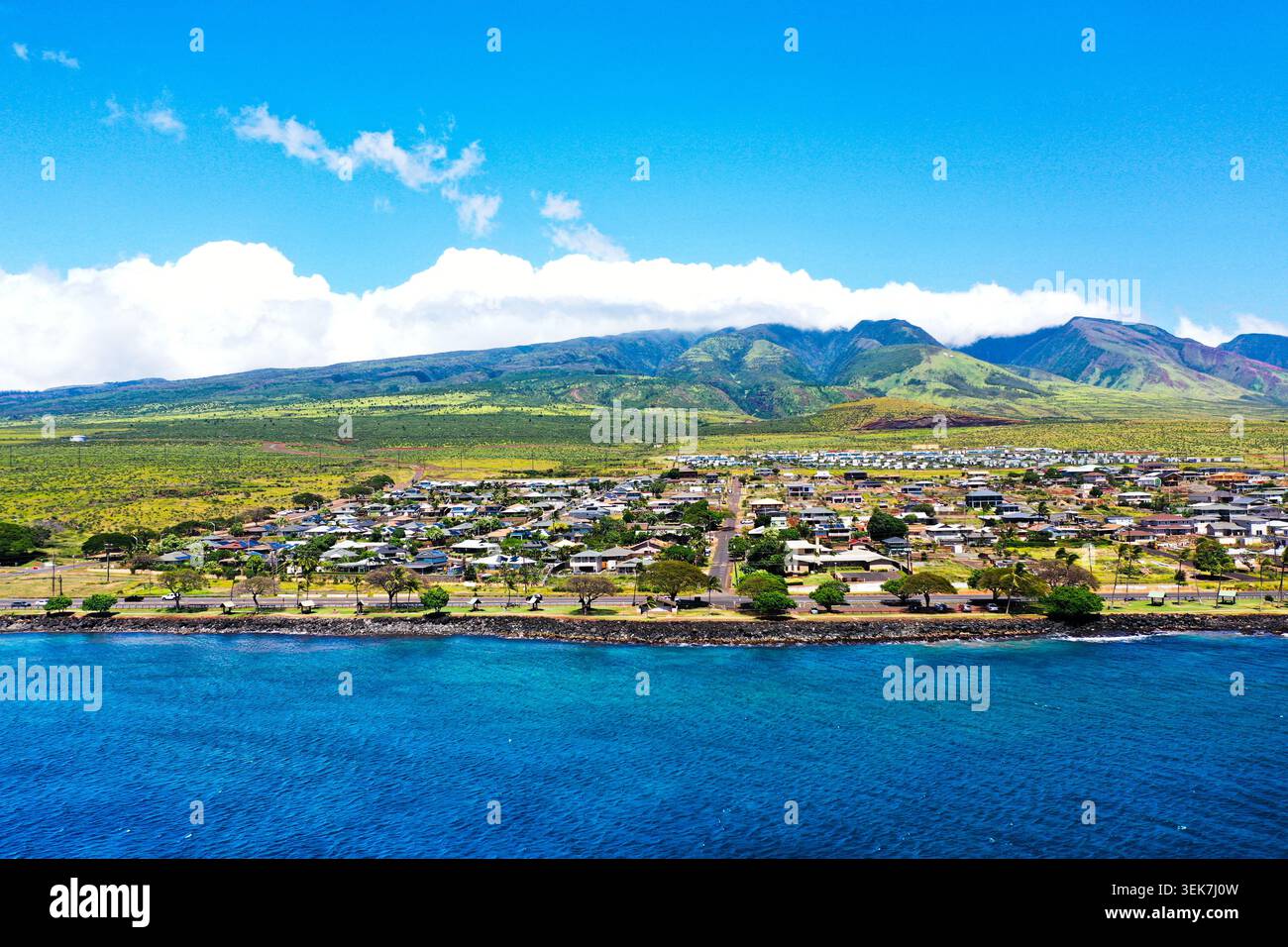 Una vista aerea della città di Lahaina situata lungo il litorale con le splendide montagne di West Maui sullo sfondo. Il vivace oceano blu contrasta Foto Stock