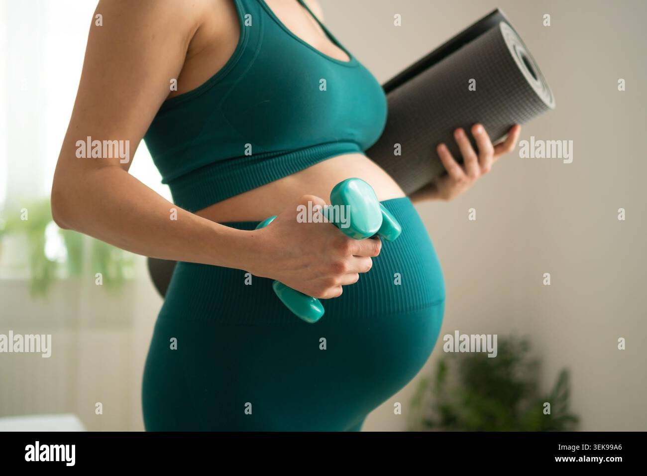 Si aspetta che la madre stia in piedi con il manubrio per l'allenamento attivo di forza in gravidanza. Donna incinta che mostra determinazione a rimanere in forma. La mamma che si prepara a combinare pesi leggeri per una routine di fitness prenatale Foto Stock