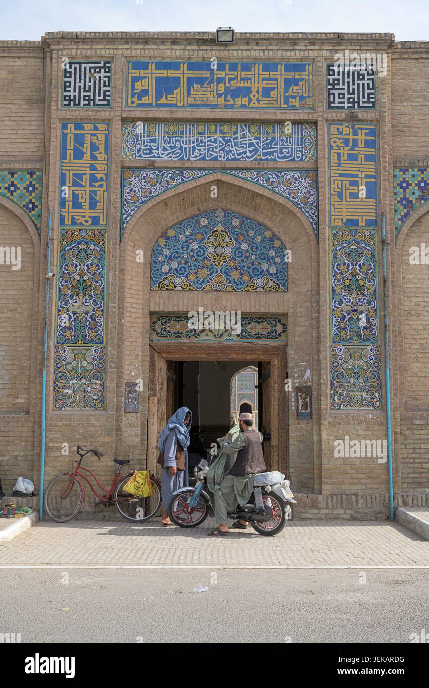 Persone che interagiscono vicino all'ingresso della grande moschea di Herat, con design islamico afgano, piastrelle decorative e calligrafia. Foto Stock