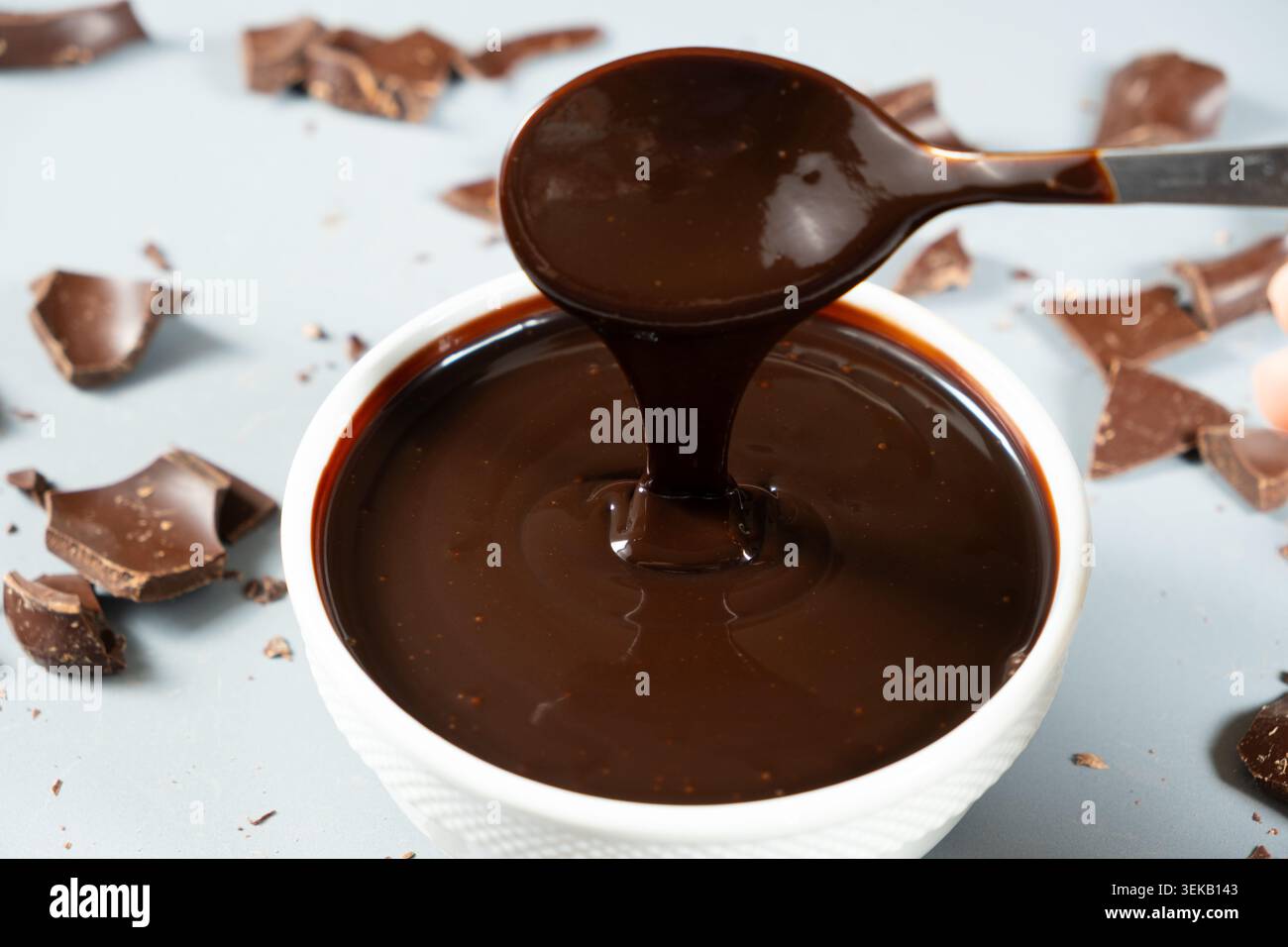 Versare lo sciroppo di cioccolato lucido dal cucchiaio. Foto Stock