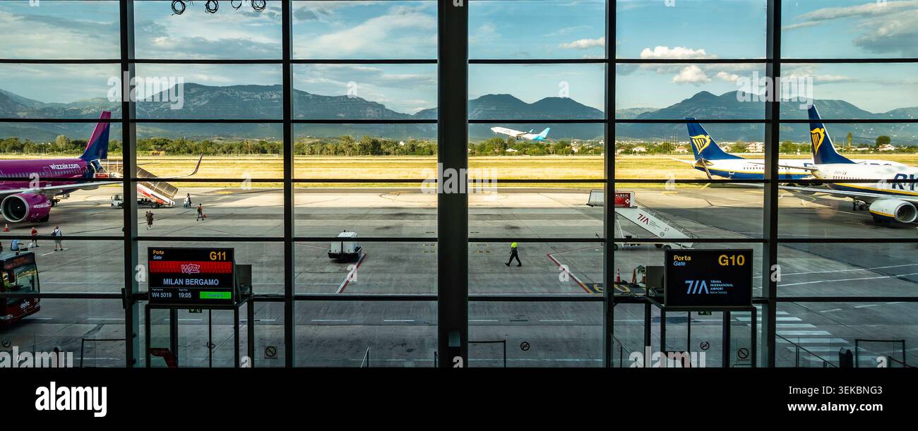 L'aeroporto internazionale di Tirana in Albania, visto attraverso le finestre del terminal, mostrava gli aerei sull'asfalto, i cancelli G10 e G11 e le montagne lontane. Foto Stock