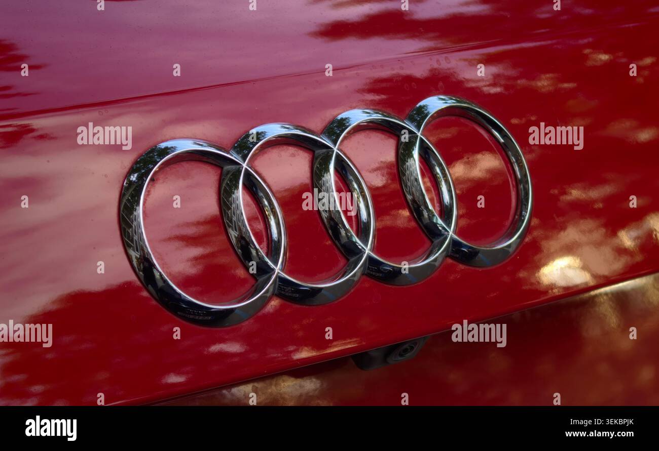 Logo Audi dettagliato montato su un'auto di colore rosso lucido con riflessi. Foto Stock