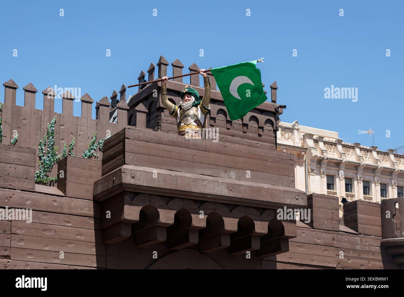 Ambasciatore moresco che tiene la bandiera della Mezzaluna Verde sopra la sua testa sul Castello al Festival dei Mori e dei cristiani, 27 aprile 2026, Alcoy, Spagna Foto Stock