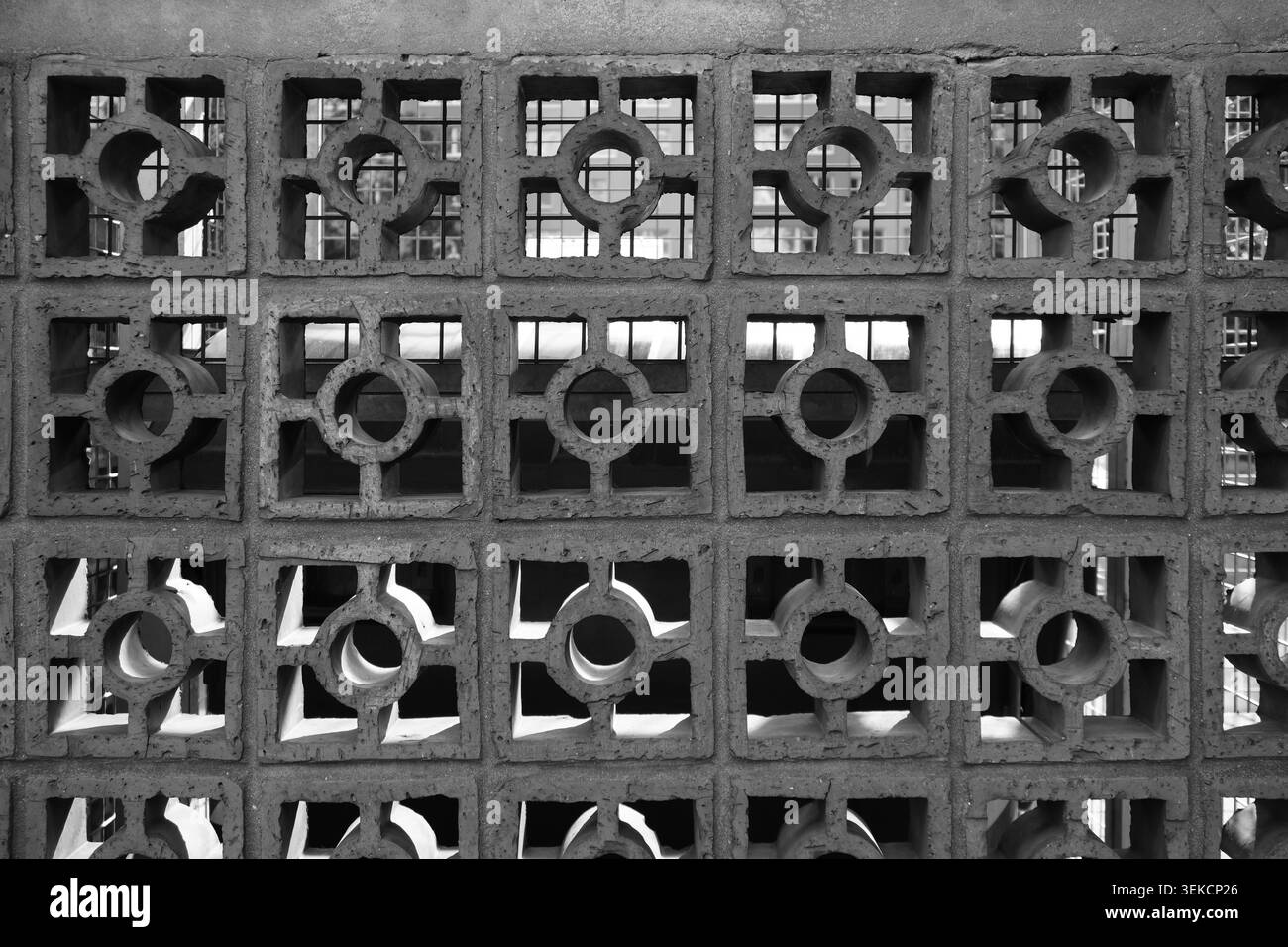 Parete in calcestruzzo monocromatico con aperture quadrate e circolari ripetute per una texture architettonica urbana. Foto Stock