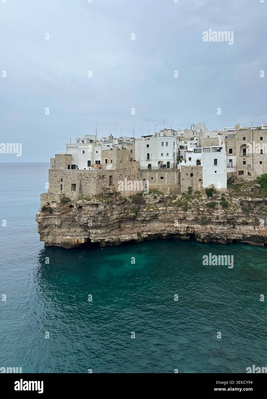 Edifici bianchi si trovano in cima a una scogliera rocciosa a Polignano a Mare, Puglia, Italia. Le strutture sono incastonate tra loro e si affacciano sul Mar Adriatico Foto Stock