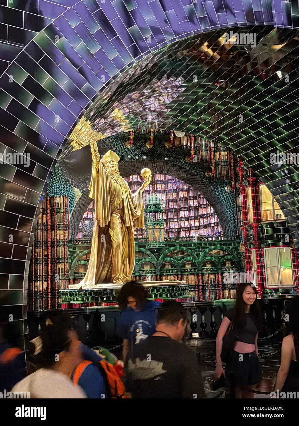 ORLANDO, FL - 1° GIUGNO 2026: Una vista interna di una torreggiante statua del mago dorato incorniciata da un arco di piastrelle verdi altamente riflettente all'interno di una coda al parco a tema Foto Stock