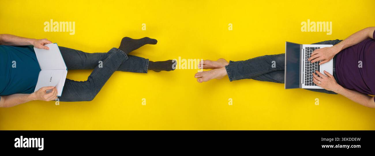 Due persone rilassate su uno sfondo giallo brillante visto dall'alto, una che usa un notebook, una che legge un libro Foto Stock