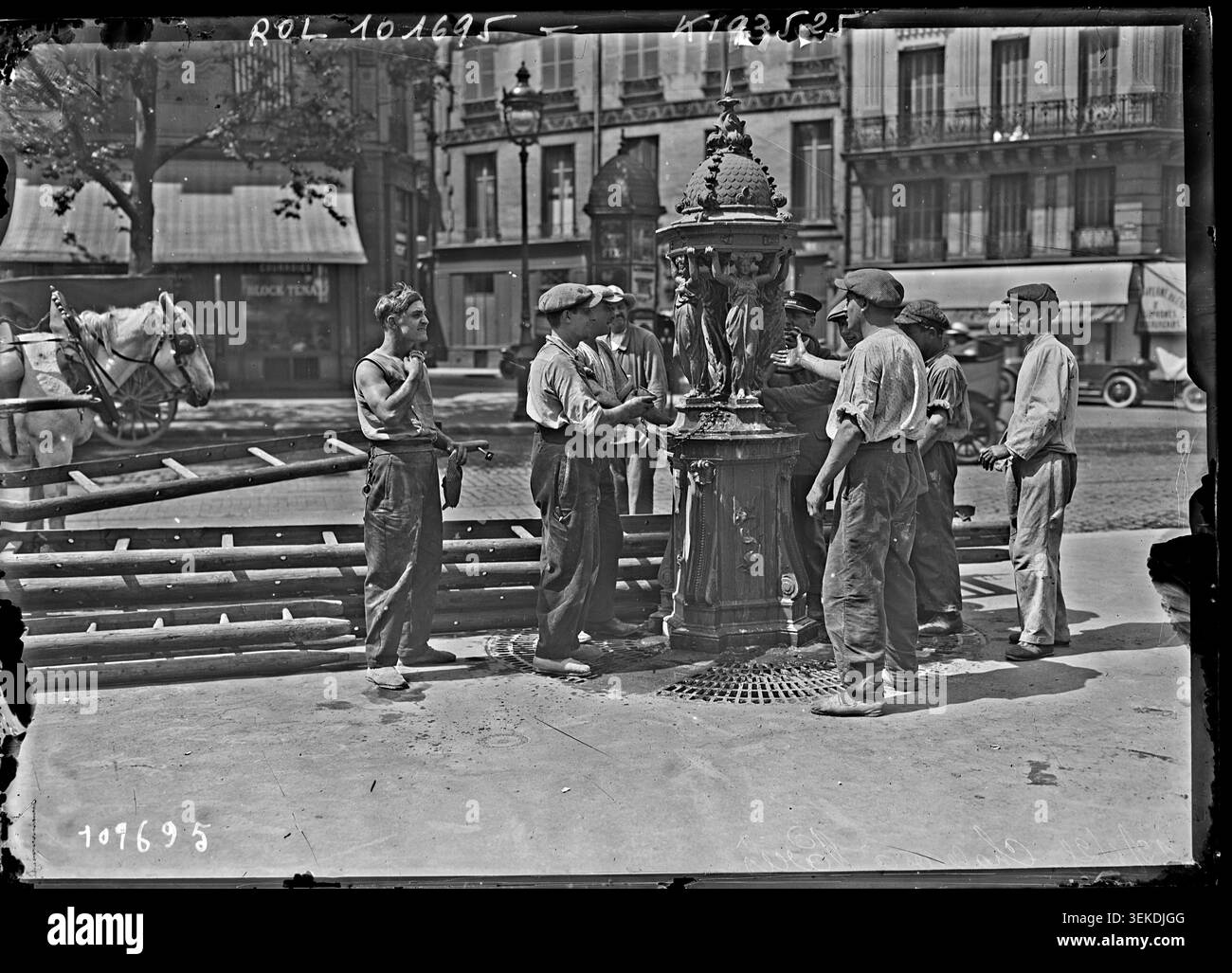 I lavoratori si riuniscono intorno a una fontana Wallace a Parigi il 12 giugno 1925 durante un periodo di caldo. Agence Rol registra la scena in una fotografia monocromatica che documenta i lavoratori e l'accesso pubblico all'acqua durante il caldo nella capitale francese. Foto Stock