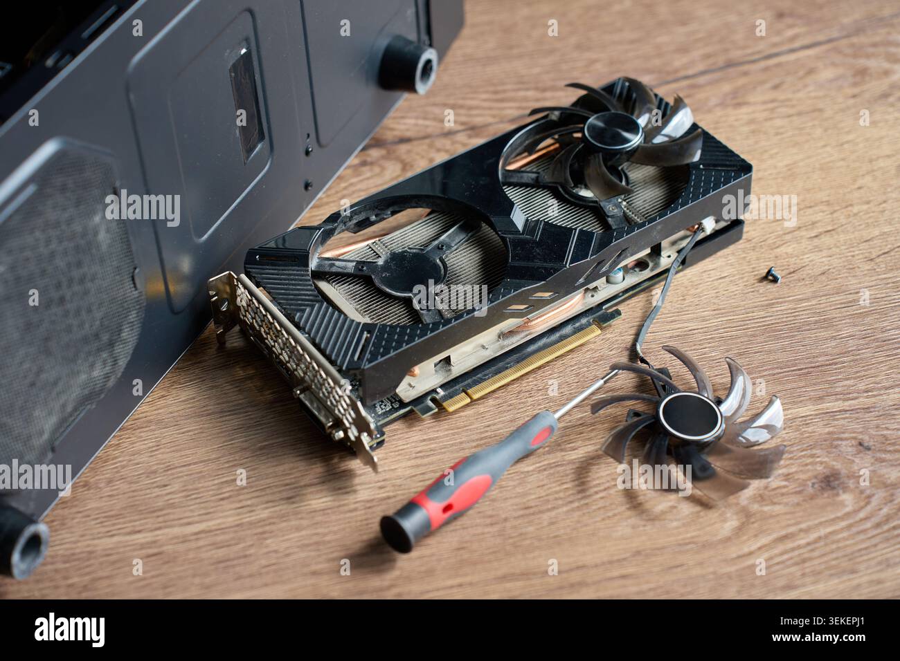 La scheda grafica smontata, la pala della ventola, il cacciavite e la vite si trovano su un tavolo di legno vicino all'alloggiamento del PC aperto. Concetto di riparazione, pulizia e manutenzione dell'hardware. Foto Stock