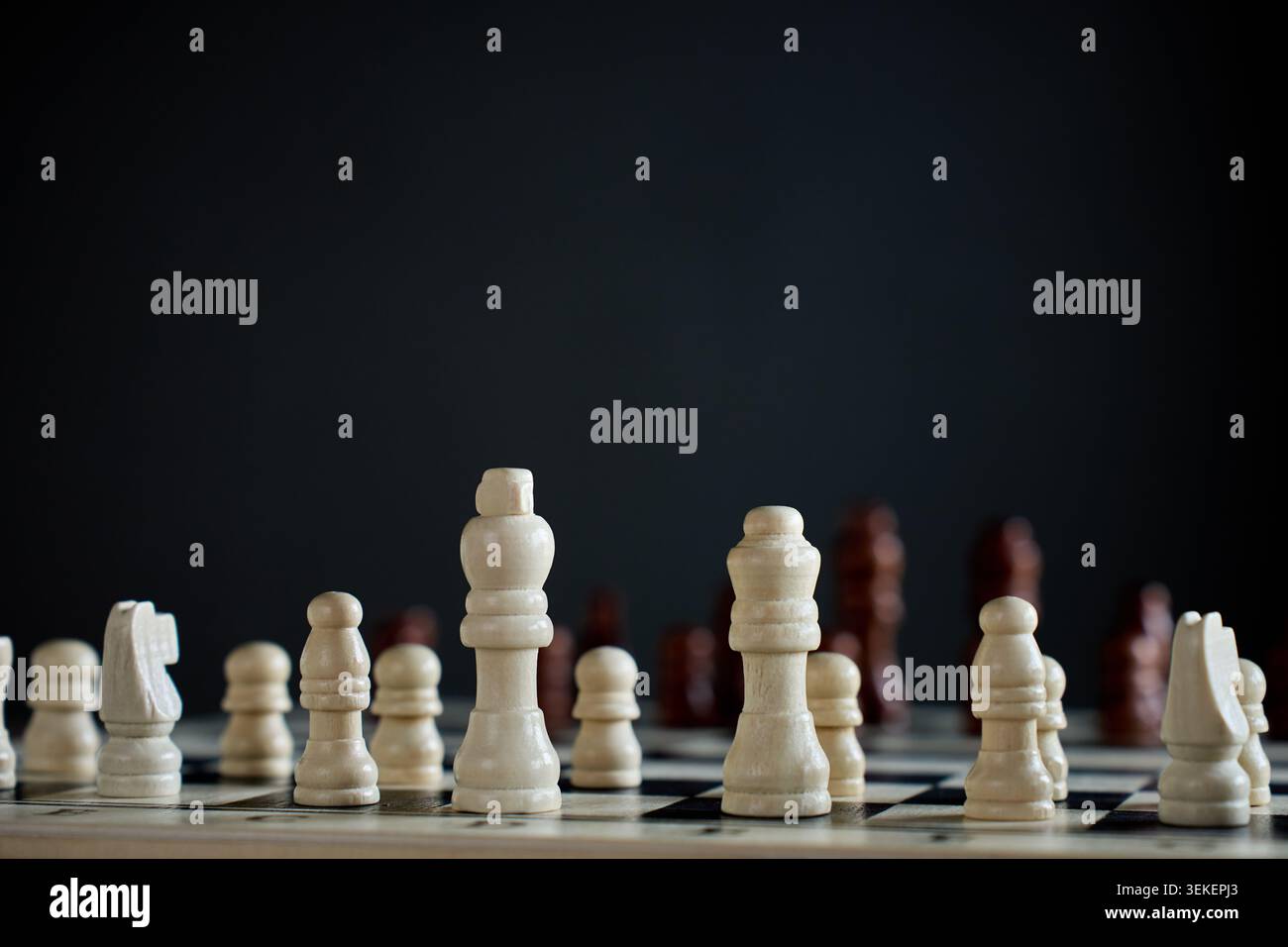 Scacchiera in legno bianco su scacchiera con pezzi neri sfocati sullo sfondo. Concetto di strategia, leadership e gioco da tavolo classico Foto Stock