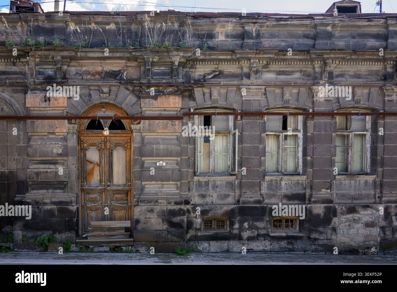 Vecchio edificio in pietra con facciata intemprata. Porta in legno e finestre rotte. Il muschio cresce su pareti e tetti. La struttura appare abbandonata e in decadimento. Foto Stock