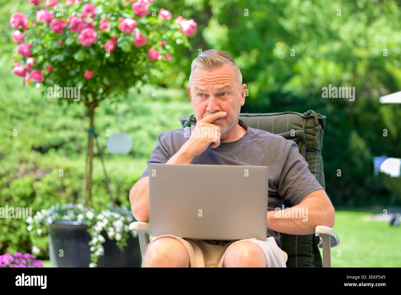 Uomo maturo che lavora con cura su un notebook mentre si rilassa all'aperto in uno splendido giardino verde. Immagine naturale dello stile di vita che rappresenta il lavoro remoto, onl Foto Stock