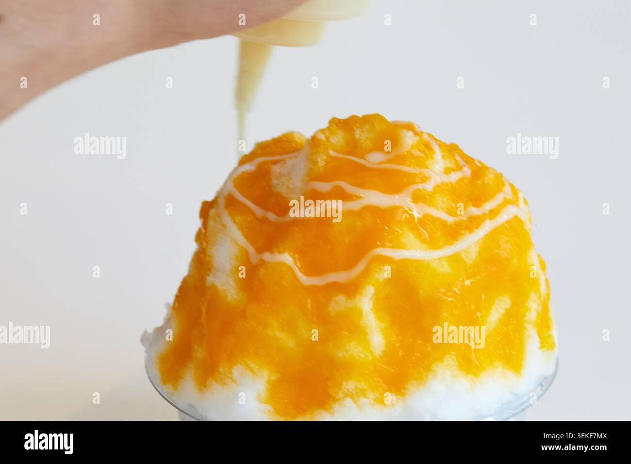 Primo piano del dessert di ghiaccio rasato al mango e condito con salsa cremosa su sfondo bianco. Foto Stock