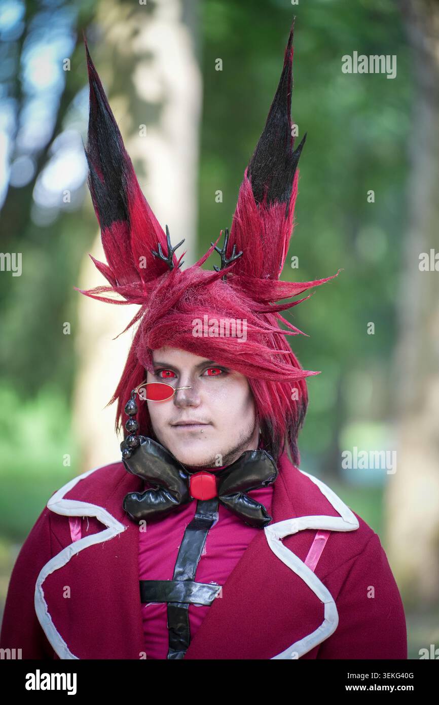 Un ritratto ravvicinato di un cosplayer vestito come il personaggio Alastor dell'Hazbin Hotel, con capelli rossi e neri stilizzati, lenti a contatto rosse, un mo Foto Stock