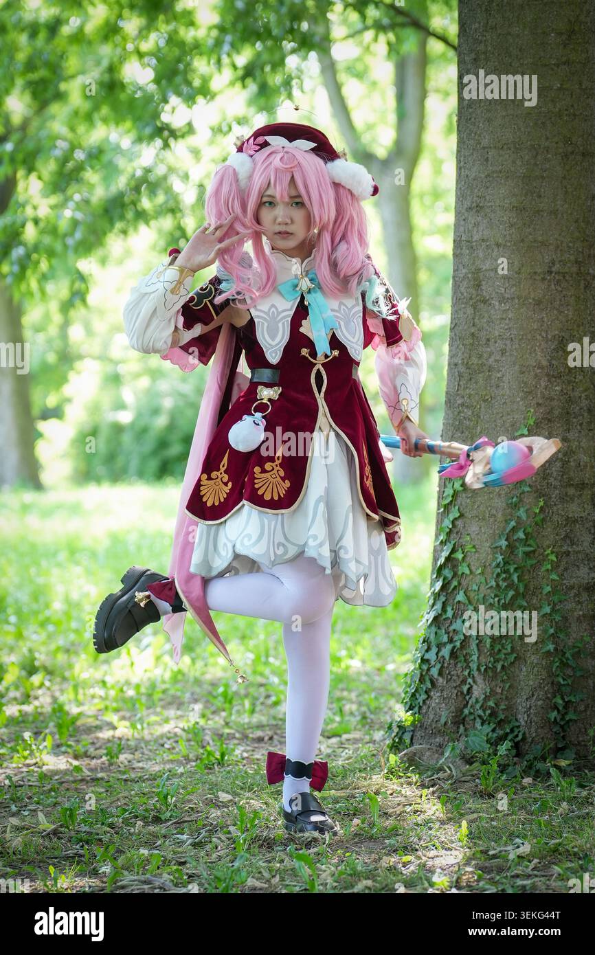 Un ritratto a figura intera di un cosplayer vestito con un abito fantasia bianco e Bordeaux ornato con una parrucca rosa, che tiene in mano un bastone decorativo mentre posa Foto Stock