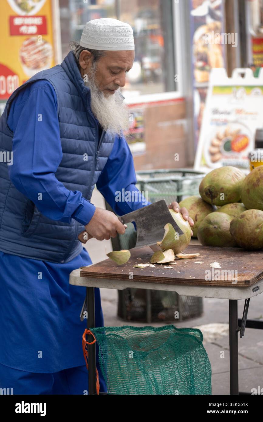 Un immigrato del Bangladesh prepara latte di cocco fresco tagliandovi l'ingresso. In Diversity Plaza, Jackson Heights, Queens, New York. Foto Stock