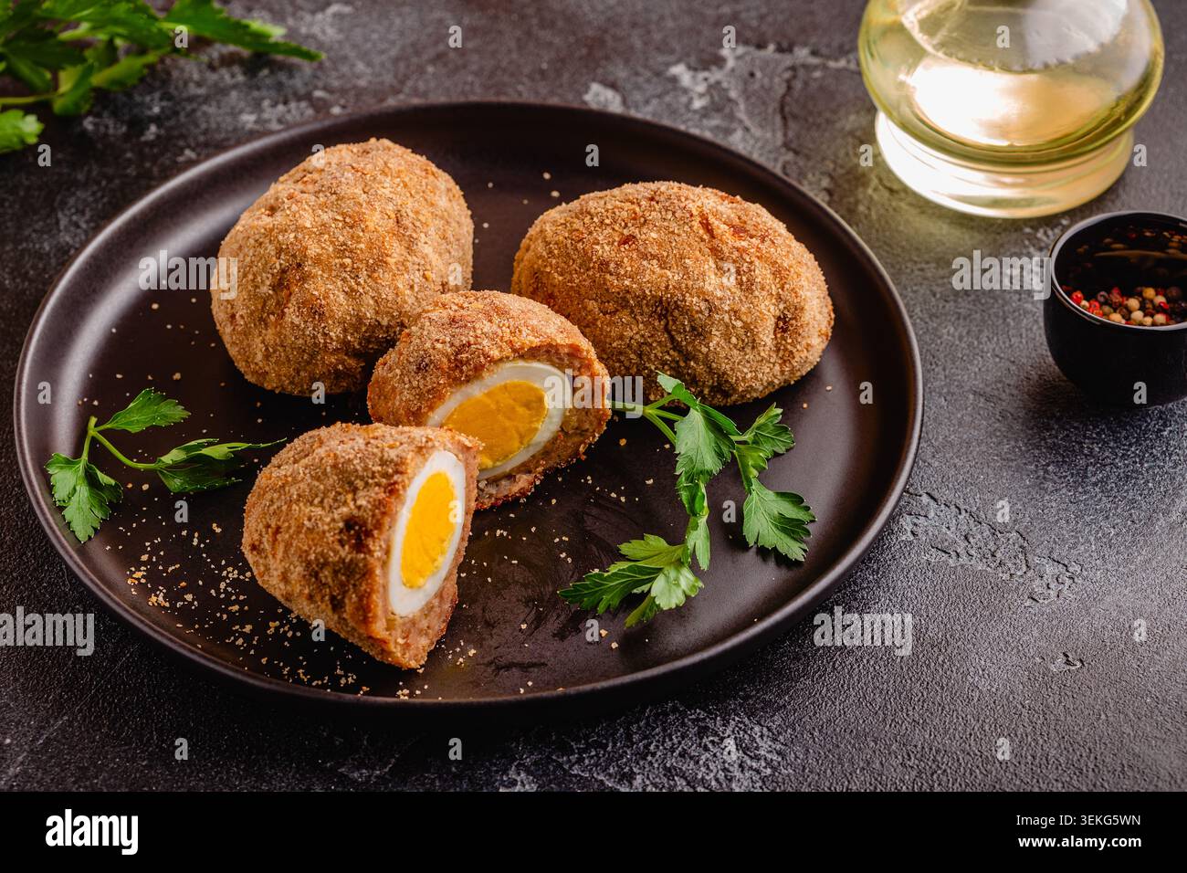 Uova tradizionali di Scotch su un piatto nero, su sfondo scuro. Foto Stock