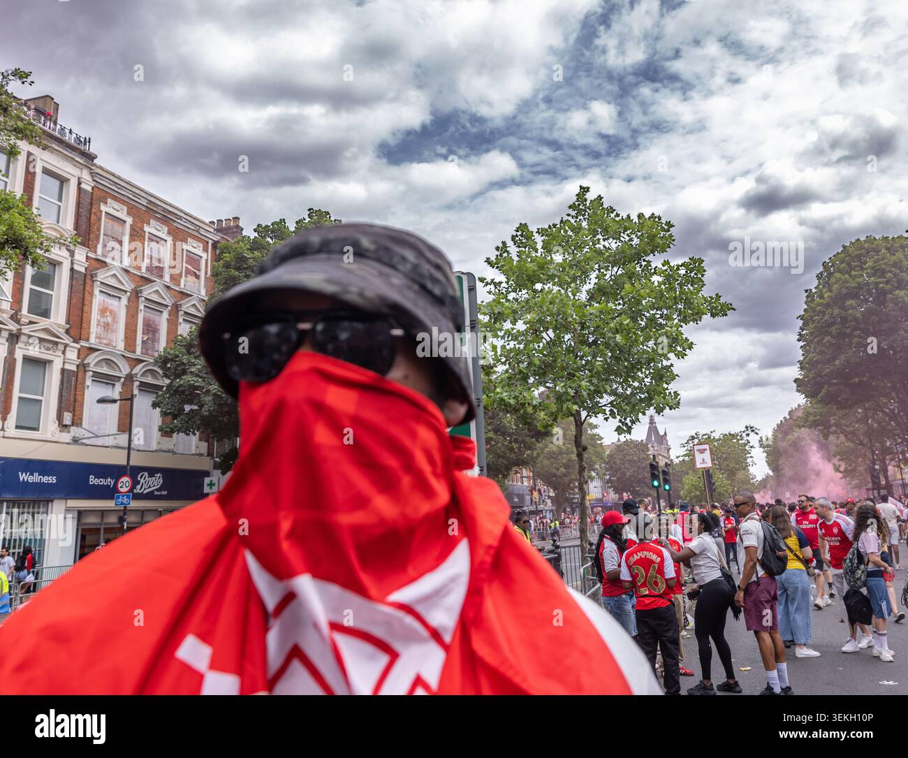 Un fan dell'Arsenal F.C. con maschera di bandiera si unisce alla folla in una strada a nord di Londra per celebrare la parata della vittoria della Premier League del club. Foto Stock
