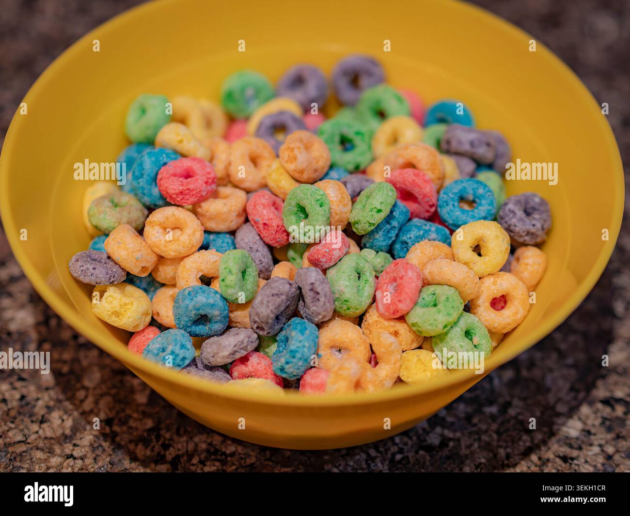 Vivaci cereali a spirale multicolore serviti in un recipiente di plastica giallo brillante su uno sfondo ruvido del piano di lavoro della cucina Foto Stock