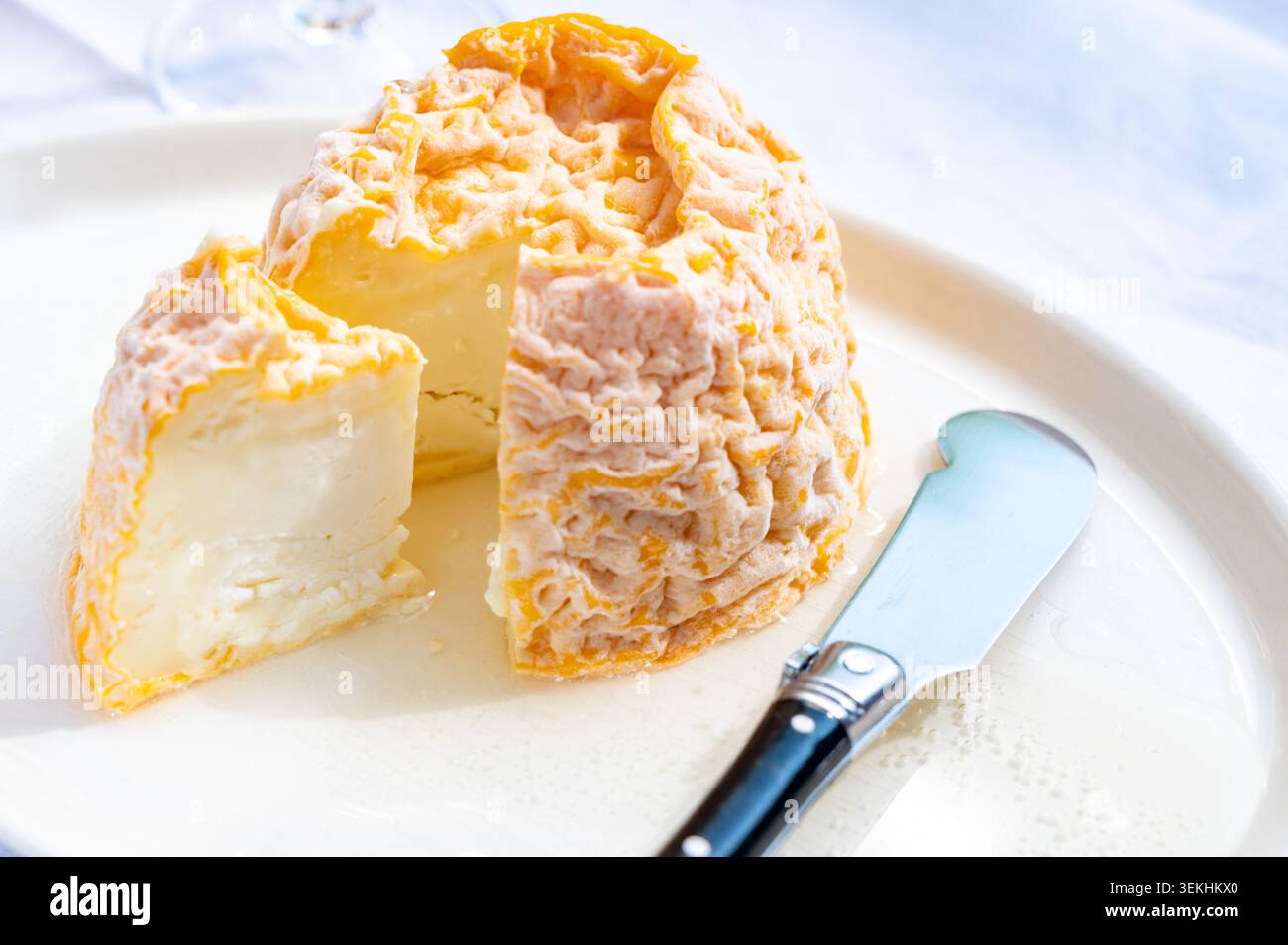 Piccolo formaggio Lsoft francese Langres rotondo con crosta lavata all'arancia e centro cremoso su un tavolo, cucchiaio e abbinato a champagne Foto Stock