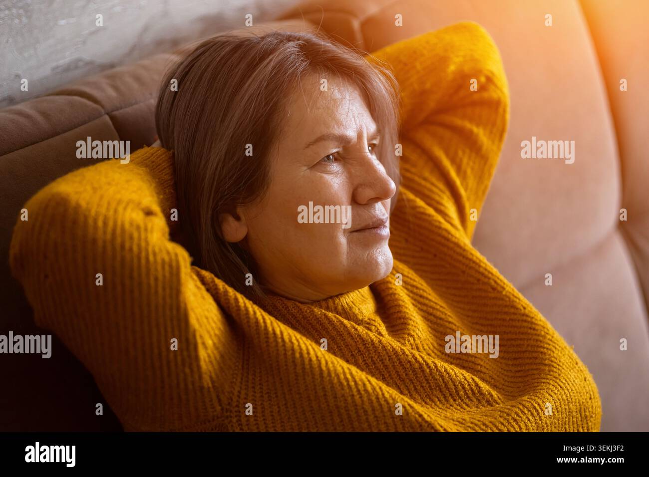 Una donna anziana premurosa che si rilassa sul divano di casa con una calda luce pomeridiana Foto Stock