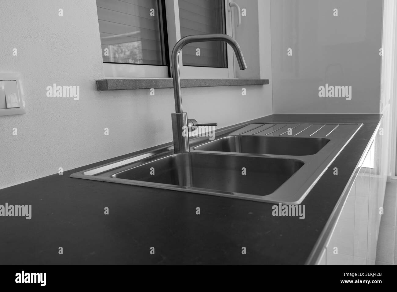 Un moderno spazio di lavoro in cucina con doppio lavabo in acciaio inossidabile, rubinetto ad arco alto e ripiano in laminato scuro Foto Stock