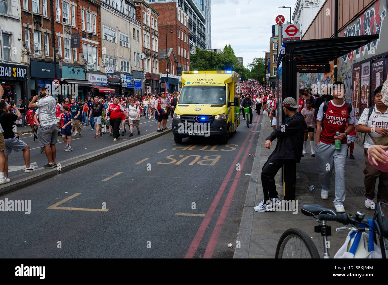 Un'ambulanza londinese su una call-out si fa strada attraverso la folla dei tifosi dell'Arsenale mentre si disperdono dopo la sfilata camminando lungo le strade principali Foto Stock