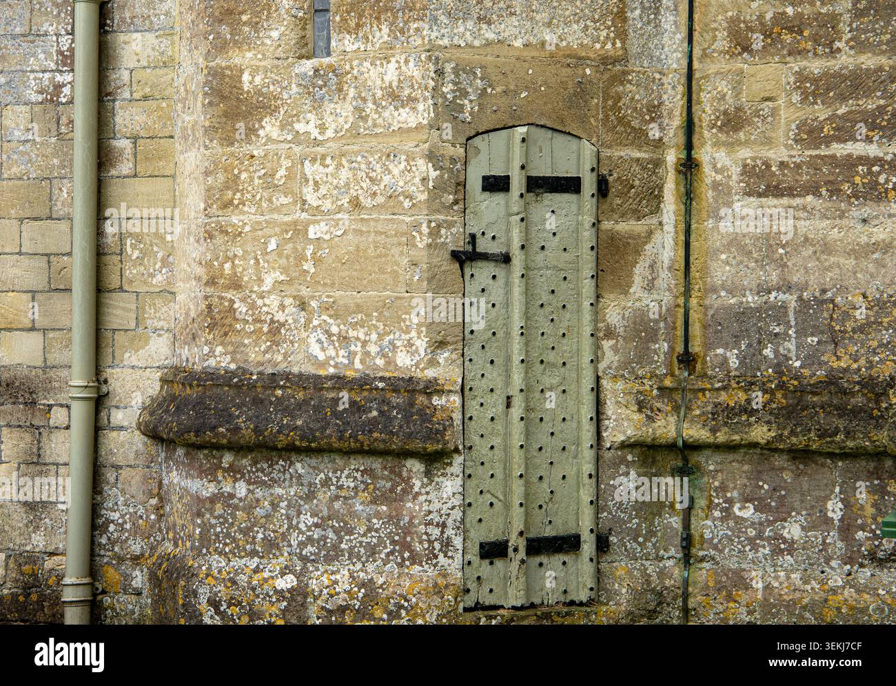 Una stretta porta in legno intemprato con borchie in metallo su un'antica parete di chiesa in pietra con muratura testurizzata Long Newton Church Gloucestershire Foto Stock