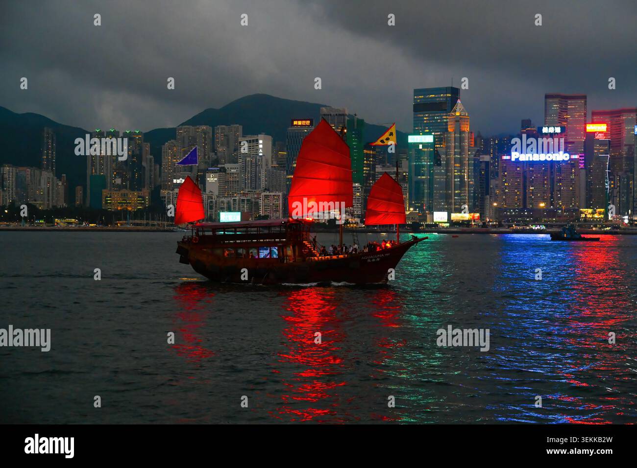 HONG KONG, CINA, 21 aprile 2026, una tradizionale imbarcazione cinese cinese Aqua Luna con iconiche vele rosse attraversa il Victoria Harbour al tramonto davanti a una sosta Foto Stock
