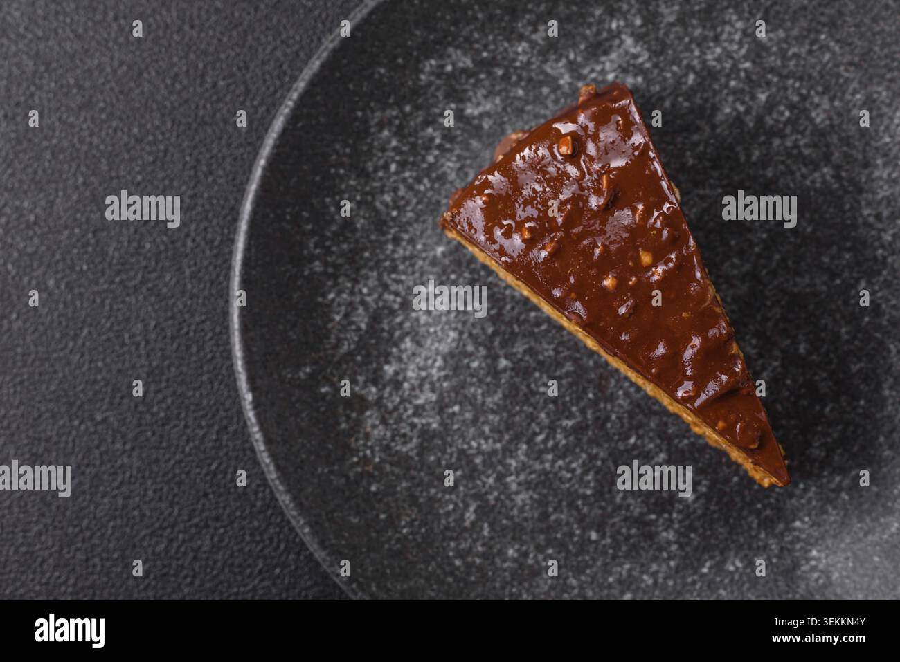 Una fetta di torta dolce a strati ricoperta di cioccolato con noci e caramello. Una fetta di torta al cioccolato come sfondo alimentare per il tuo design Foto Stock