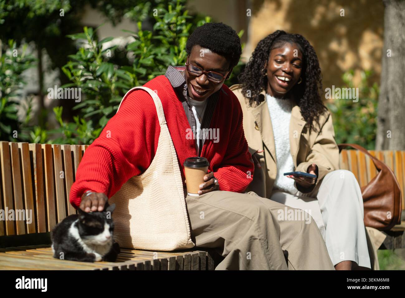 Felice amico afroamericano uomo donna che si gode compagnia di gatto randagio mentre riposa sulla panchina del parco Foto Stock