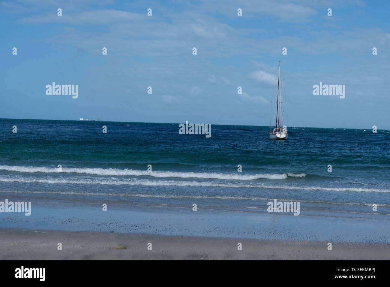 Barca a vela ancorata al largo di Smugglers Bay vicino a Whangarei, Nuova Zelanda, con onde gentili e una vasta spiaggia sabbiosa sotto un cielo blu. Foto Stock