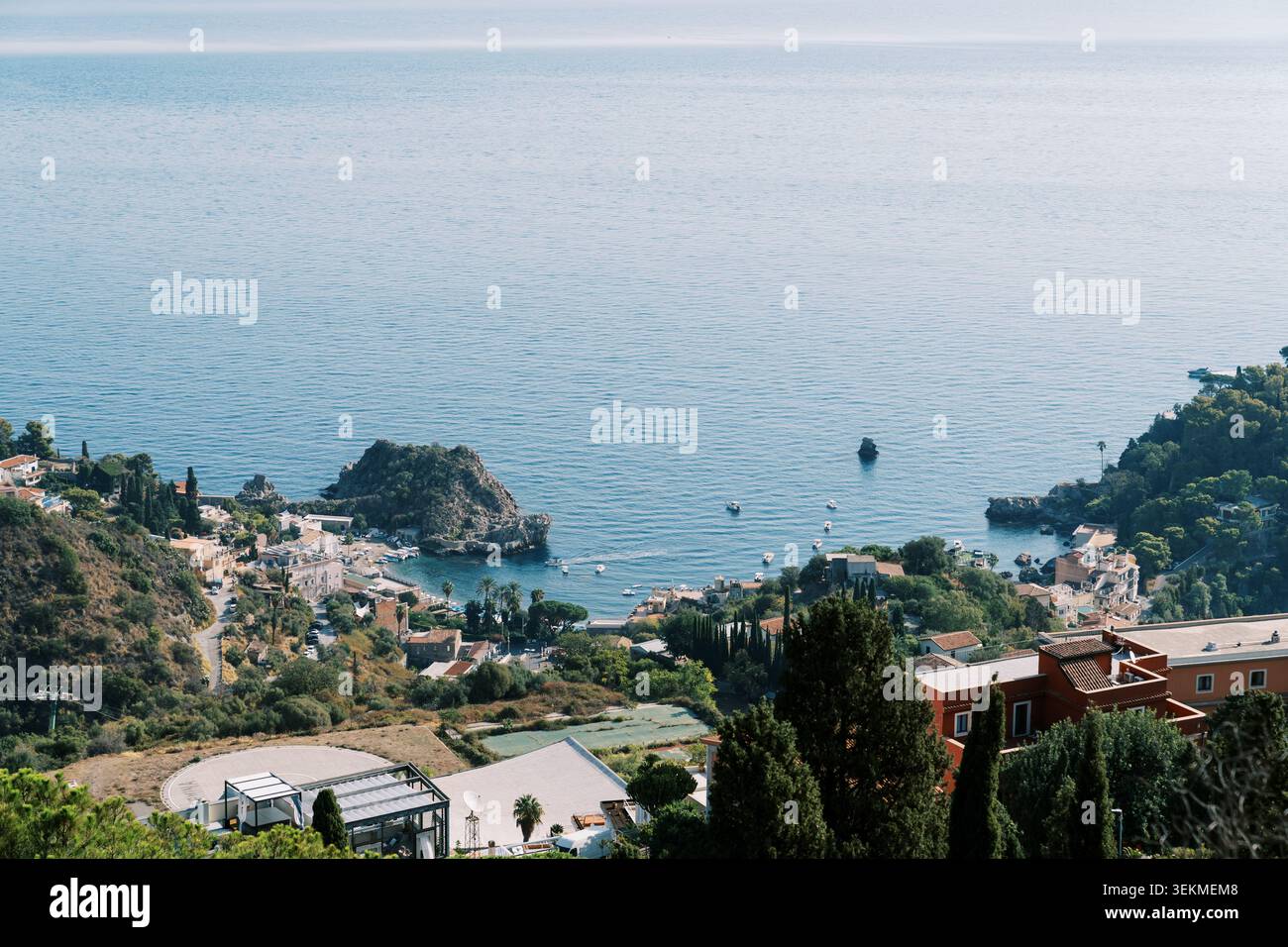 Tranquillo villaggio costiero con mura in pietra e lussureggianti dintorni di pini Foto Stock