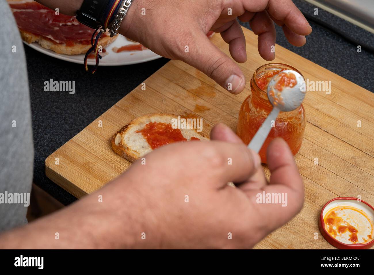 Persona che distribuisce la marmellata di pomodoro sul pane tostato per uno spuntino o un pasto Foto Stock