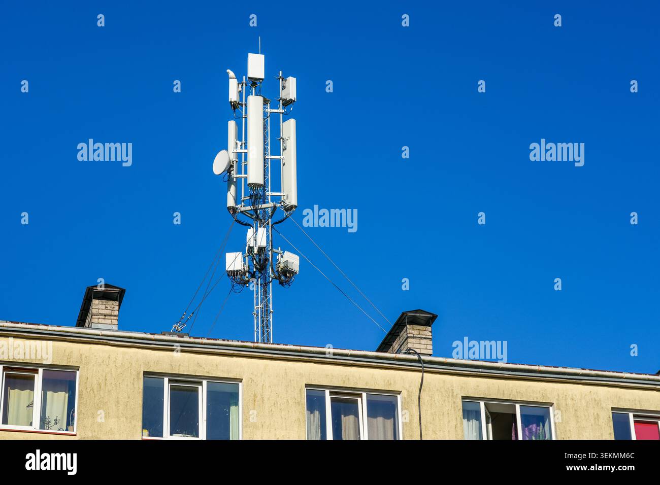 Torre di comunicazione cellulare montata sul tetto di un edificio residenziale sullo sfondo del cielo azzurro Foto Stock