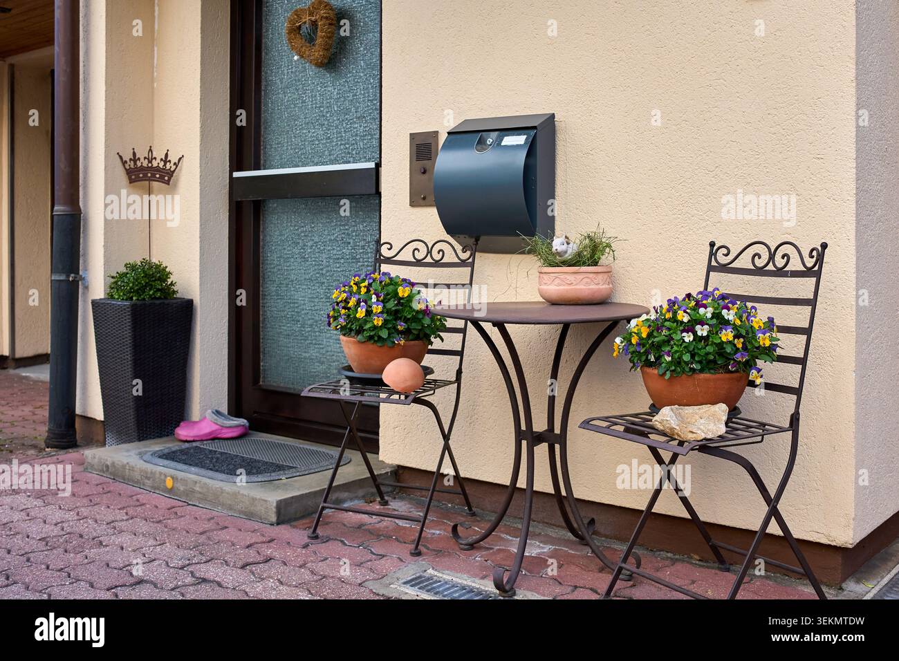 Accogliente area d'ingresso a casa decorata con un tavolo da bistrot in metallo, sedie, colorati fiori viola in vaso e una moderna cassetta postale a parete. Foto Stock