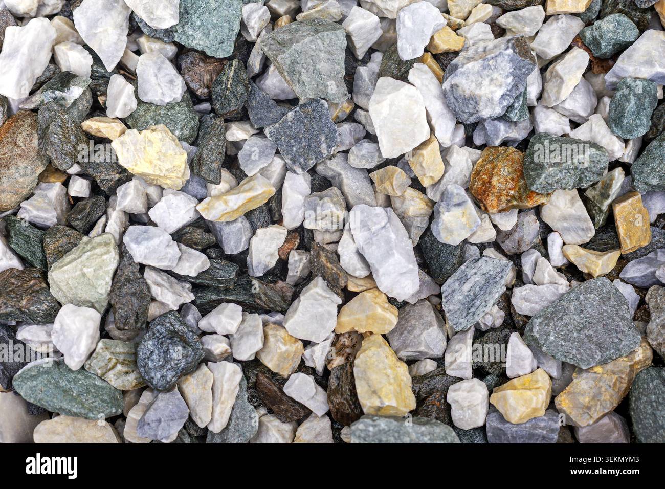 Fondo misto di pietre di ghiaia. Vista ravvicinata di pietre di ghiaia ruvida assortite nei toni bianco, grigio, verde e giallo per una texture naturale Foto Stock