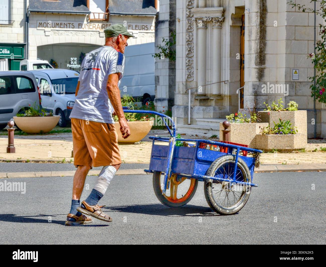 Uomo anziano con una gamba fasciata che spinge un carro a mano per la città - Ligueil, Indre-et-Loire (37), Francia. Foto Stock