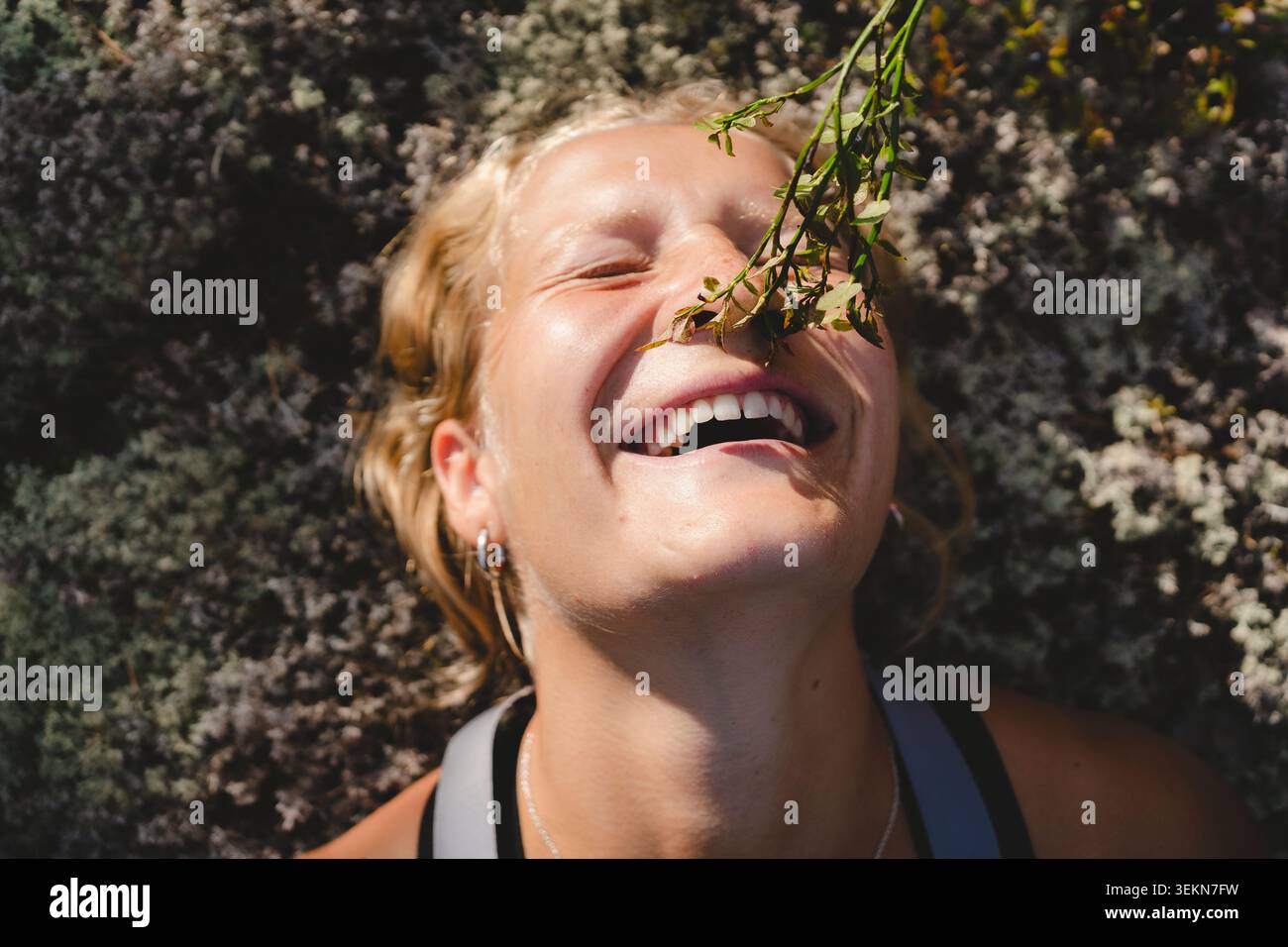 Vista ravvicinata di una donna felice con gli occhi chiusi sdraiati sui fiori nelle giornate di sole Foto Stock