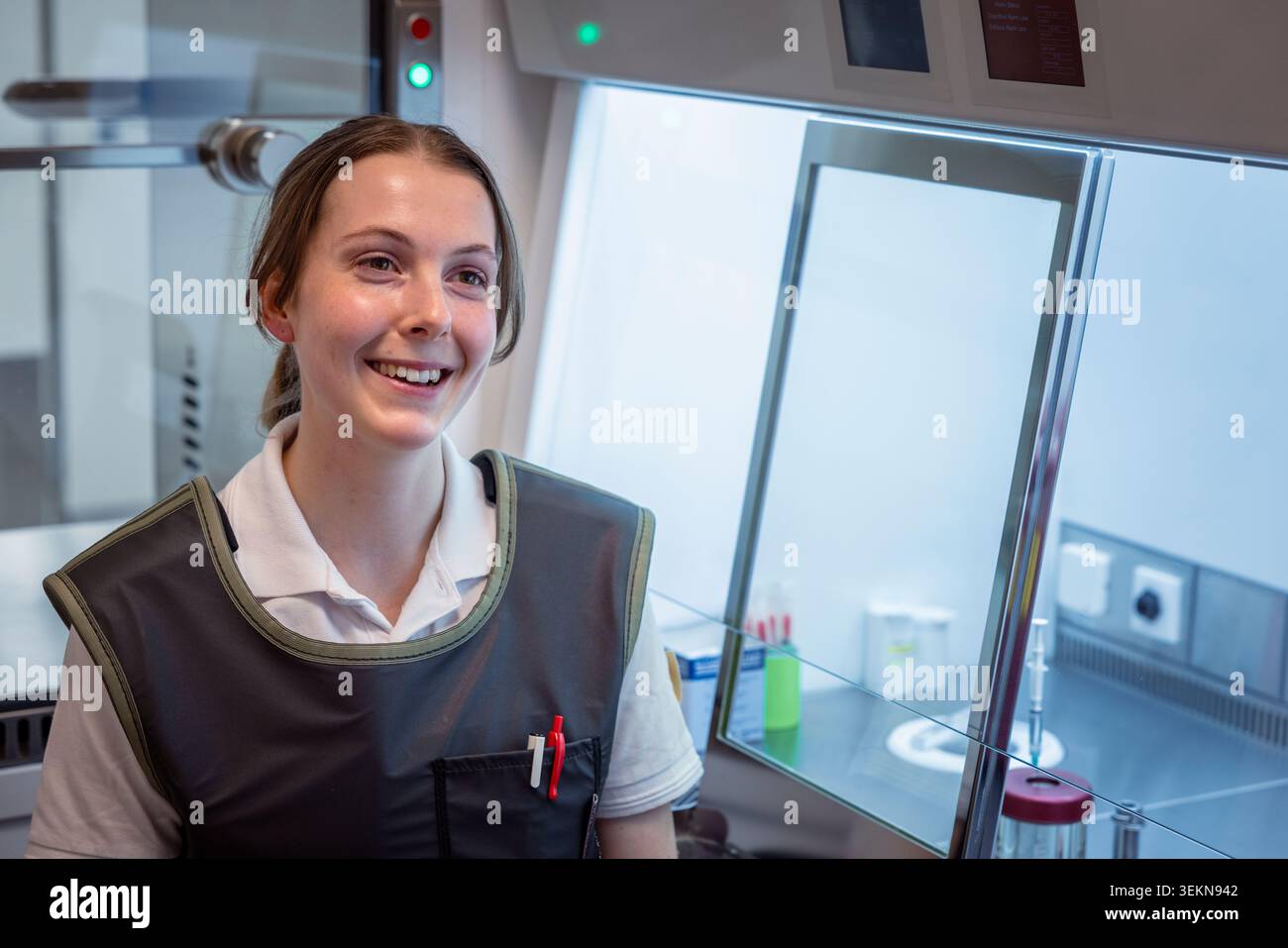 Scienziata sorridente che guarda lontano mentre è seduta nel laboratorio di ricerca Foto Stock