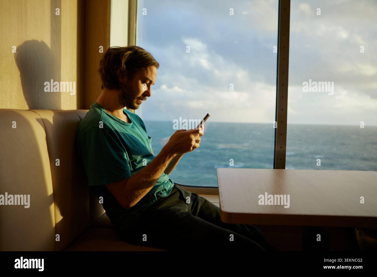 Uomo che usa lo smartphone mentre siede vicino alla finestra in traghetto Foto Stock