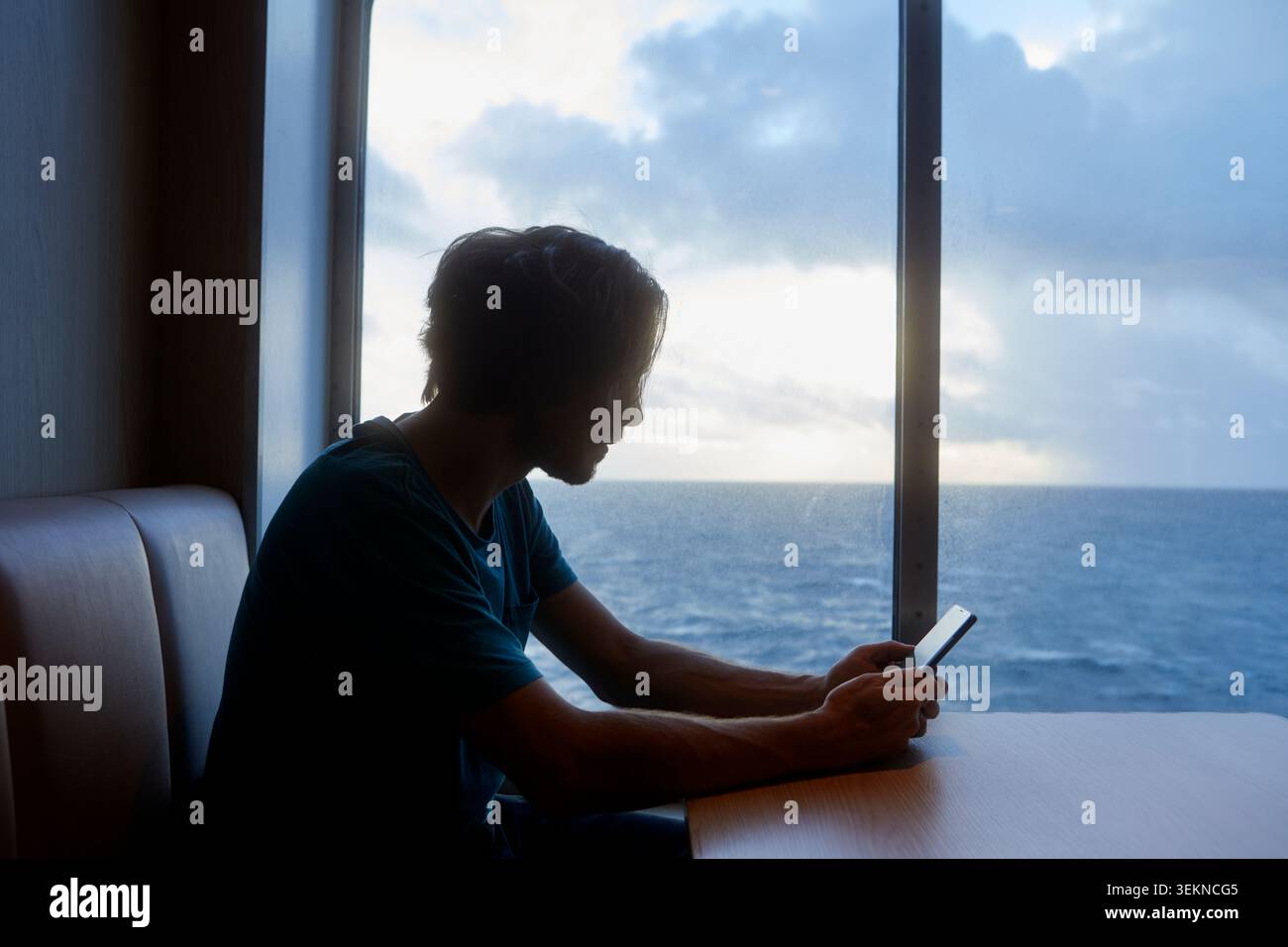 Uomo che utilizza uno smartphone seduto vicino alla finestra sul traghetto Foto Stock