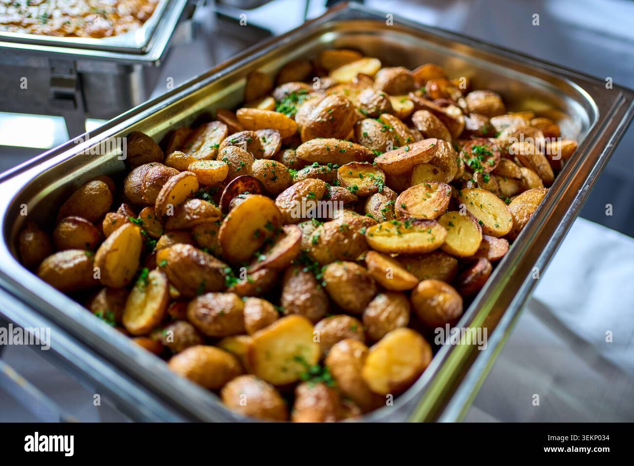Un piatto a fette di metallo ripieno di patate croccanti arrostite condite con erbe aromatiche presso una postazione di ristorazione a buffet. Foto Stock