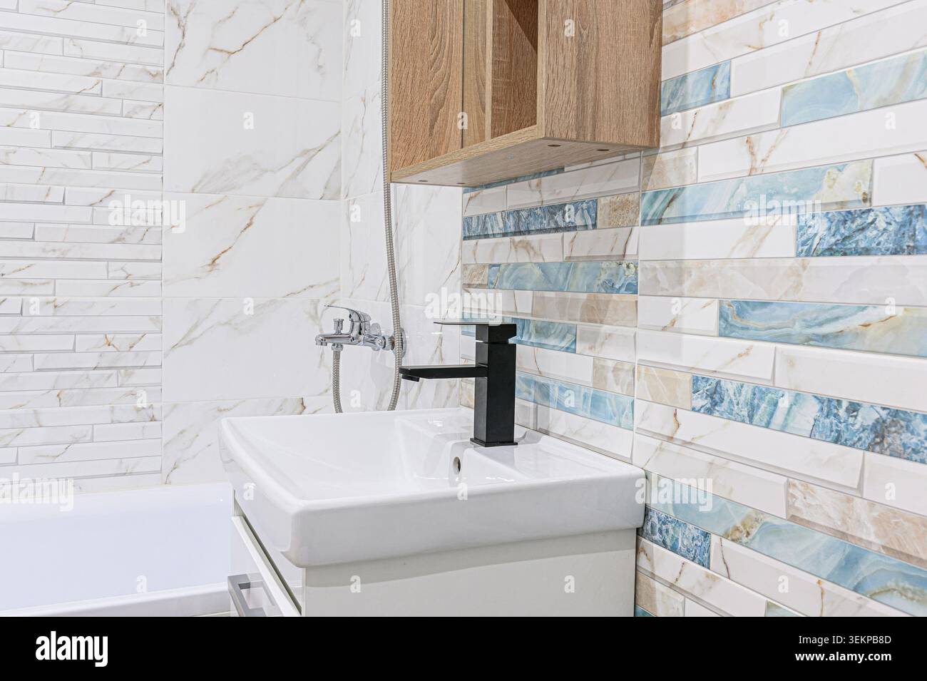 bagno moderno con lavandino bianco con rubinetto nero e wc bianco su una parete piastrellata con dettagli blu e beige. Foto Stock