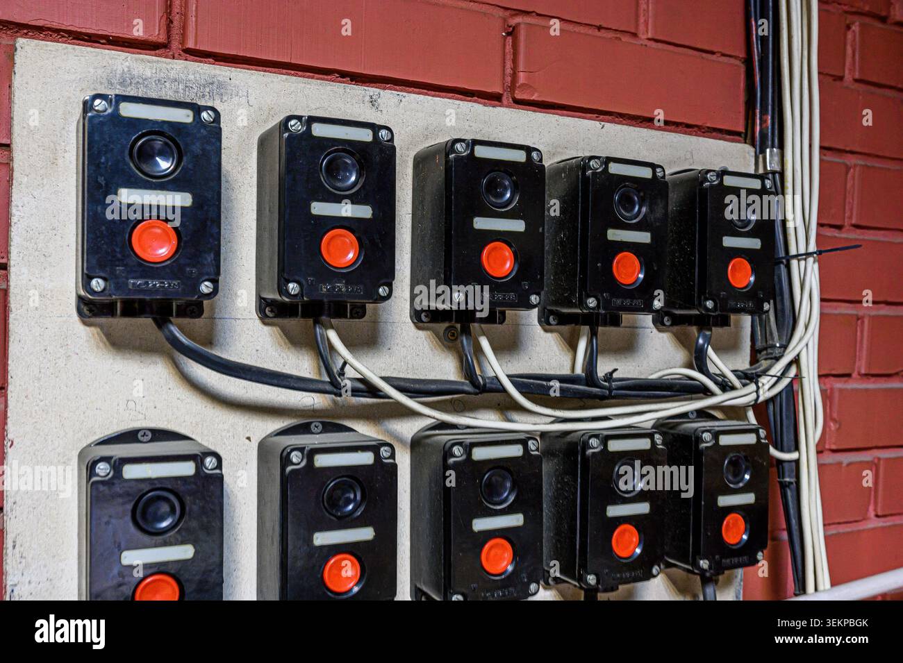 set di pulsanti elettrici o interruttori montati su una parete, con contenitori neri, pulsanti rossi e cablaggio visibile, posizionati contro una parete in mattoni Foto Stock