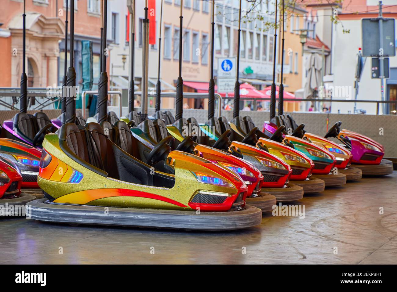 Una fila di autoscontri colorati parcheggiati in una pista vuota del parco divertimenti in un'ambientazione europea di festival di strada. Foto Stock