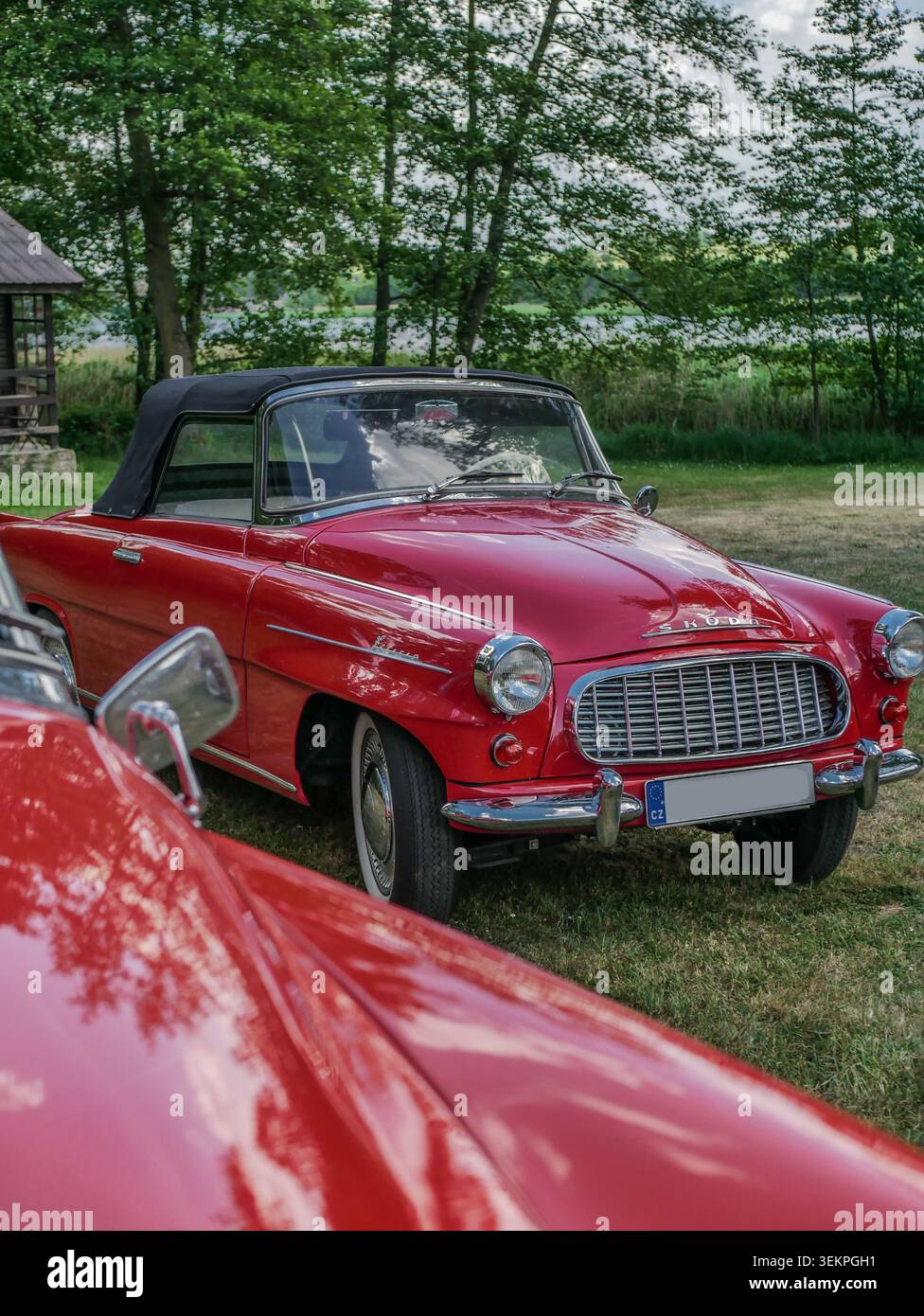 Vista anteriore di tre quarti di una classica cabriolet rossa fotografata sopra il cofano di un altro veicolo. Forte enfasi sulla cromatura e sulle linee della carrozzeria. Foto Stock