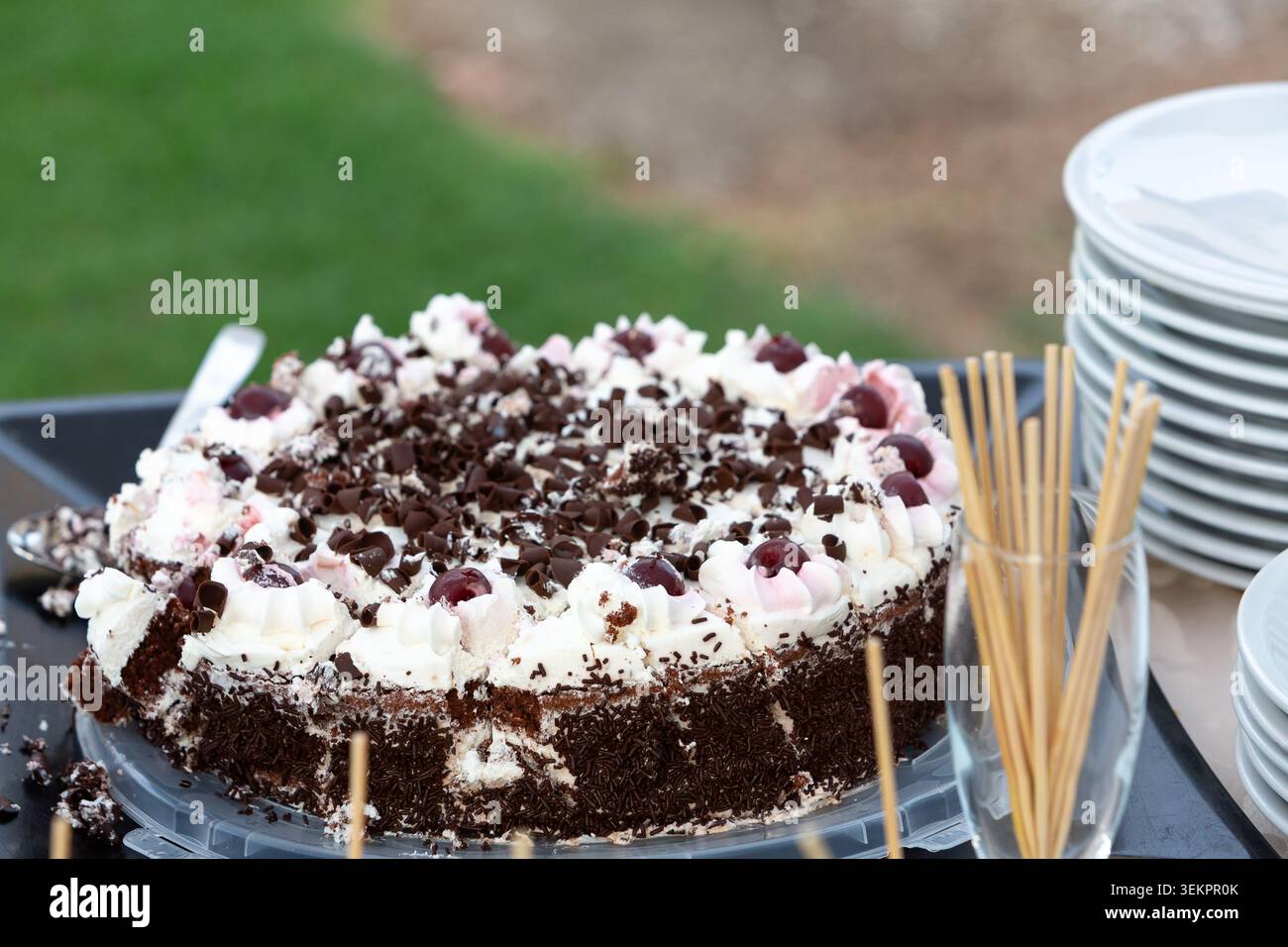 Torta foresta nera con scaglie di cioccolato e ciliegie su un tavolo accanto a piatti e spiedini impilati Foto Stock